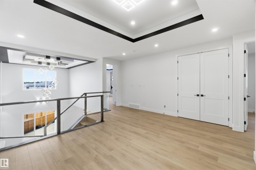 Spacious interior landing featuring light wood-finish flooring, a contemporary chandelier, recessed ceiling lighting, and a modern glass and metal railing system - 417 Pine Point(E), Leduc, AB - Indoor Photo Showing Other Room