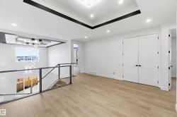 Spacious interior landing featuring light wood-finish flooring, a contemporary chandelier, recessed ceiling lighting, and a modern glass and metal railing system - 