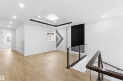 Open concept upper-level hallway featuring light wood-finish flooring, a contemporary staircase with glass railing, recessed lighting, and a tray ceiling with a modern light fixture - 