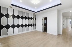 Open concept room featuring a decorative accent wall with geometric paneling, wood-finish flooring, a recessed tray ceiling with integrated lighting, and modern pendant light fixtures - 