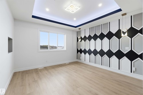 Accent wall featuring geometric paneling, wood-finish flooring, a recessed ceiling with perimeter lighting, a multi-pane window, and two pendant light fixtures - 417 Pine Point(E), Leduc, AB - Indoor Photo Showing Other Room