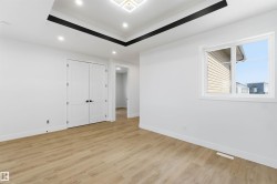 Spacious room featuring wood-finish flooring, white walls, and a tray ceiling with recessed lighting - 