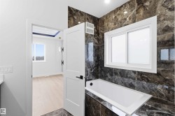 Bathroom featuring a built-in tub with dark marble-look tile surround and a sliding window - 