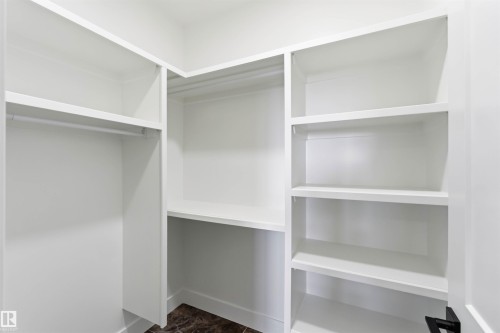 Walk-in closet featuring white built-in shelving, hanging rods, and dark patterned flooring - 417 Pine Point(E), Leduc, AB - Indoor With Storage