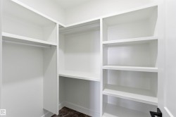 Walk-in closet featuring white built-in shelving, hanging rods, and dark patterned flooring - 