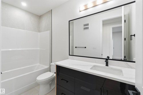 Bathroom featuring a white tub/shower combination with light-colored tile surround, a toilet, a dark vanity with a white countertop, and a large mirror with a matte black frame - 417 Pine Point(E), Leduc, AB - Indoor Photo Showing Bathroom