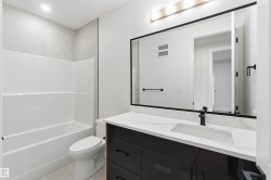 Bathroom featuring a white tub/shower combination with light-colored tile surround, a toilet, a dark vanity with a white countertop, and a large mirror with a matte black frame - 
