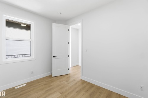 Bright interior space featuring a window with white trim, wood-finish flooring, white walls, a white paneled door with black hardware, and white baseboards - 417 Pine Point(E), Leduc, AB - Indoor Photo Showing Other Room