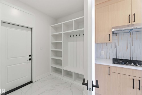Entryway featuring a white paneled door with matte black hardware, built-in white storage shelving, and white marble-look tile flooring - 415 Pine Point(E), Leduc, AB - Indoor