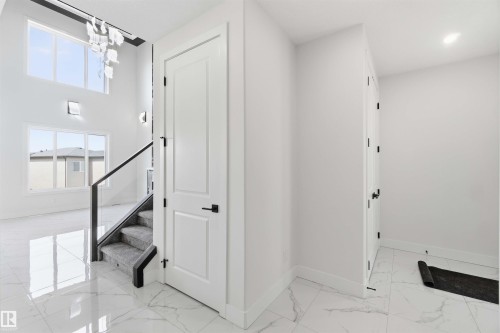 Two-story foyer featuring large windows, a contemporary chandelier, a staircase with glass railing and carpeted treads, and polished marble-look tile flooring - 415 Pine Point(E), Leduc, AB - Indoor Photo Showing Other Room