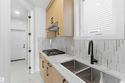 Kitchenette featuring light wood-finish cabinetry with matte black hardware, a gas cooktop, a double basin stainless steel sink with a matte black faucet, and white countertops - 415 Pine Point(E), Leduc, AB - Indoor Photo Showing Kitchen