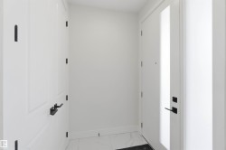 Entryway featuring a white paneled door with matte black hardware, a frosted glass sidelight, and white tile flooring - 