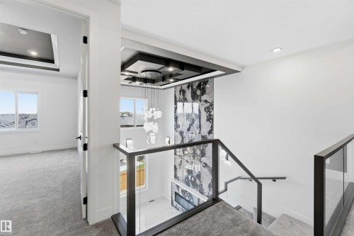 Modern staircase featuring glass panel railings with dark frames, a textured feature wall, and a multi-tiered chandelier - 415 Pine Point(E), Leduc, AB - Indoor Photo Showing Other Room