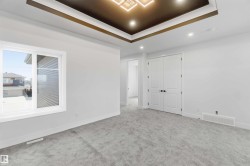 Spacious room featuring light gray carpeting, crisp white walls, and a recessed tray ceiling with an integrated modern light fixture - 