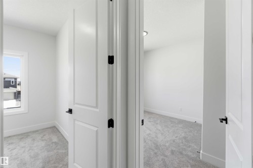 Two rooms featuring light gray carpeting, crisp white walls, and modern white paneled doors with matte black hardware - 415 Pine Point(E), Leduc, AB - Indoor Photo Showing Other Room