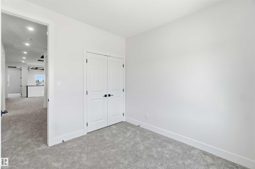 Bright room with light gray carpeting, white walls, and a double-door closet featuring matte black hardware - 415 Pine Point(E), Leduc, AB - Indoor Photo Showing Other Room