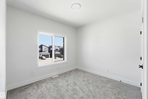 Bright interior space featuring a double-pane window, light gray carpet, white baseboards, and a circular flush-mount ceiling light - 415 Pine Point(E), Leduc, AB - Indoor Photo Showing Other Room