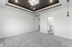 Spacious room featuring a tray ceiling with recessed lighting and a geometric chandelier, light gray carpeting, and white walls with thick baseboards - 