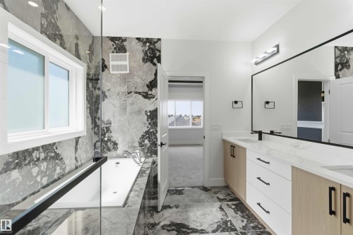 Contemporary bathroom featuring a built-in soaking tub with a glass panel enclosure, oversized vanity with dual sinks, natural wood-finish and white cabinetry, and large format stone-look tile flooring - 415 Pine Point(E), Leduc, AB - Indoor