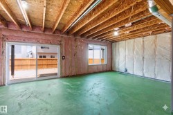 Unfinished basement with exposed ceiling joists, insulation-ready walls, a sliding glass door, and an additional window - 