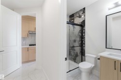 Bathroom featuring a walk-in shower with black-framed glass enclosure, dark veined tile surround, and a light wood-finish vanity with white countertop - 