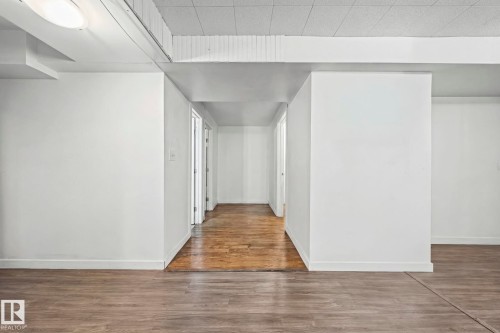 This interior space features light-colored walls and a blend of two distinct flooring types: a grey wood-look flooring and a rich brown wood flooring - 115 Warwick Road, Edmonton, AB - Indoor Photo Showing Other Room