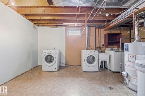 The property features a laundry area with a washer, a dryer, and a utility sink, all set on tiled flooring - 115 Warwick Road, Edmonton, AB - Indoor Photo Showing Laundry Room