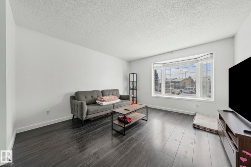 The living area features dark wood-style flooring, white walls, and a large bay window - 115 Warwick Road, Edmonton, AB - Indoor Photo Showing Living Room