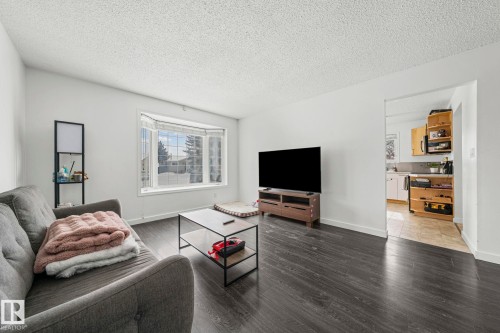 The living area features dark wood-style flooring and a large bay window, providing natural light - 115 Warwick Road, Edmonton, AB - Indoor Photo Showing Living Room