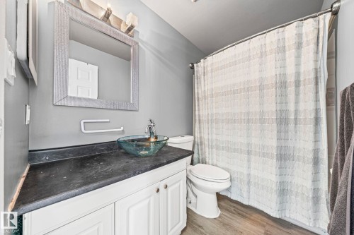 Bathroom featuring a vessel sink, a vanity with white cabinetry, a shower with a patterned curtain, and wood-style flooring - 115 Warwick Road, Edmonton, AB - Indoor Photo Showing Bathroom