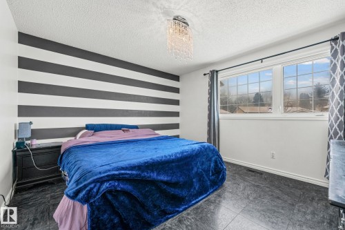 This bedroom features a window with exterior views, dark flooring, and a decorative ceiling light fixture - 115 Warwick Road, Edmonton, AB - Indoor Photo Showing Bedroom