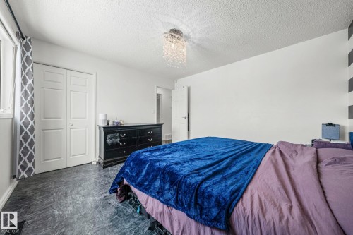 Bedroom featuring a textured ceiling, a window with patterned curtains, and double bifold closet doors - 115 Warwick Road, Edmonton, AB - Indoor Photo Showing Bedroom