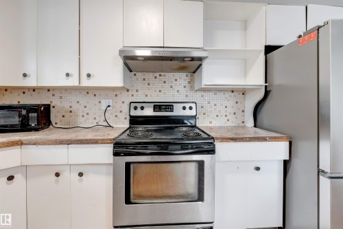 Kitchen featuring appliances with stainless steel finishes, white cabinetry, under cabinet range hood, backsplash, and open shelves - 12202 45 Street, Edmonton, AB - Indoor Photo Showing Kitchen