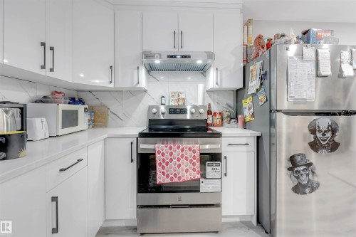 Kitchen with appliances with stainless steel finishes, white cabinets, decorative backsplash, and range hood - 12202 45 Street, Edmonton, AB - Indoor Photo Showing Kitchen
