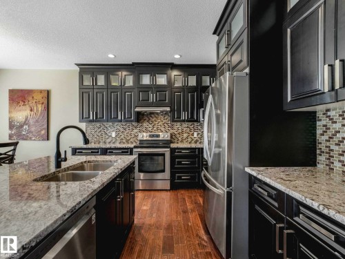 Kitchen with dark wood cabinetry, light-toned granite countertops, and a mosaic tile backsplash - 16251 135 Street Nw, Edmonton, AB - Indoor Photo Showing Kitchen With Stainless Steel Kitchen With Double Sink With Upgraded Kitchen