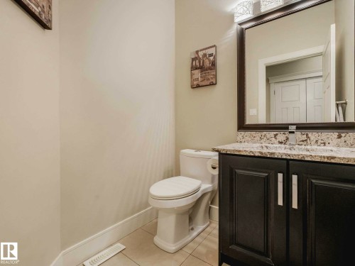 Bathroom featuring a dark wood vanity with a light speckled countertop, framed mirror, and a three-light vanity fixture - 16251 135 Street Nw, Edmonton, AB - Indoor Photo Showing Bathroom