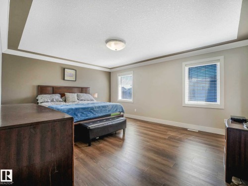 Spacious room featuring tray ceiling, wood-finish flooring, two windows, and neutral wall tones - 16251 135 Street Nw, Edmonton, AB - Indoor Photo Showing Bedroom