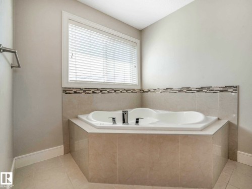 Built-in corner tub featuring deck-mounted fixtures, surrounded by large format tile, with a decorative mosaic tile accent - 16251 135 Street Nw, Edmonton, AB - Indoor Photo Showing Bathroom