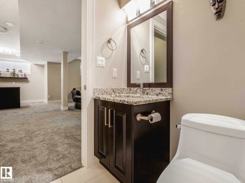 Bathroom vanity featuring a framed mirror, a granite-finish countertop, and dark wood-finish cabinetry - 16251 135 Street Nw, Edmonton, AB - Indoor Photo Showing Bathroom