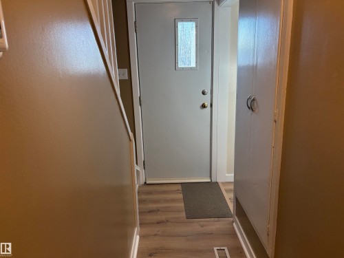 Entryway featuring a light gray door with a rectangular frosted glass insert, wood-finish flooring, and built-in white cabinetry with silver-tone hardware - 410 Main St, Alcomdale, AB - Indoor Photo Showing Other Room