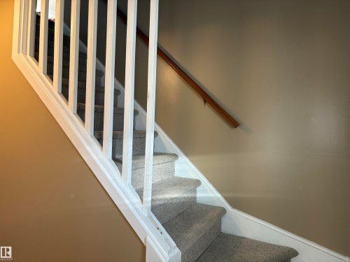 Carpeted staircase featuring white balusters and a wood handrail - 410 Main St, Alcomdale, AB - Indoor Photo Showing Other Room