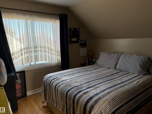 Attic bedroom featuring hardwood flooring and a window with sheer and blackout curtains - 410 Main St, Alcomdale, AB - Indoor Photo Showing Bedroom