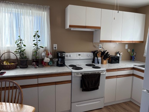 Kitchen featuring white cabinetry with wood-finish trim, white appliances, and a window with sheer curtains - 410 Main St, Alcomdale, AB - Indoor Photo Showing Kitchen