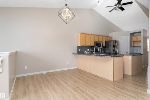 Kitchen area featuring light wood-finish cabinetry, stainless steel appliances, and a central island with a bar seating area - 15109 Miller Boulevard, Edmonton, AB - Indoor Photo Showing Kitchen