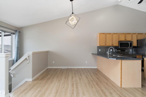 Kitchen and dining area featuring vaulted ceilings, wood-finish flooring, a contemporary geometric light fixture, wood cabinetry, and stainless steel appliances - 15109 Miller Boulevard, Edmonton, AB - Indoor Photo Showing Kitchen