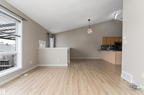 Open-concept living area featuring wood-finish flooring, vaulted ceilings, and a contemporary pendant light fixture - 15109 Miller Boulevard, Edmonton, AB - Indoor