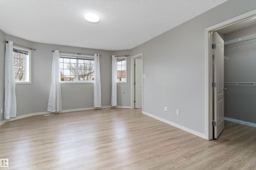 Bright room featuring wood-finish flooring, light gray wall paint, multiple windows, a flush-mount ceiling light, and a built-in closet with shelving - 15109 Miller Boulevard, Edmonton, AB - Indoor Photo Showing Other Room