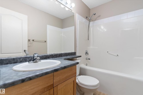 Bathroom featuring a wood-finish vanity with an integrated oval sink, a durable countertop, and a vanity-width mirror - 15109 Miller Boulevard, Edmonton, AB - Indoor Photo Showing Bathroom