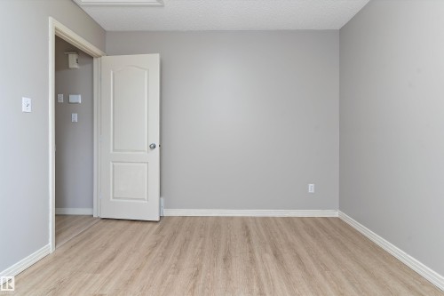 Neutral gray walls with white baseboards frame wood-finish flooring - 15109 Miller Boulevard, Edmonton, AB - Indoor Photo Showing Other Room