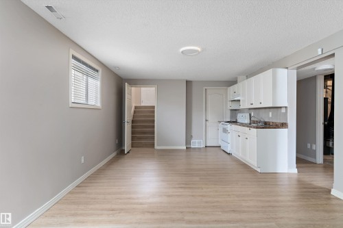 Open living area featuring wood-finish flooring, white kitchen cabinetry, a built-in oven range, a window with horizontal blinds, and a staircase - 15109 Miller Boulevard, Edmonton, AB - Indoor Photo Showing Kitchen